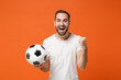© ViDi Studio - Excited young man in casual white t-shirt posing isolated on orange background studio portrait. People sincere emotions lifestyle concept. Mock up copy space. Hold soccer ball doing winner gesture.