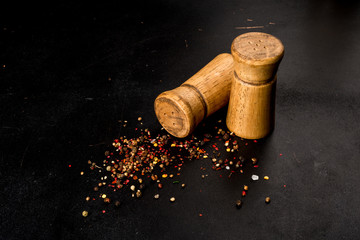 Salt and pepper in wooden salt shakers on a black background