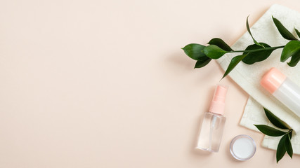 Transparent cosmetic bottle containers and cream jar on beige background with towel and green leaves. Minimal flat lay style composition, top view. Natural organic beauty product concept