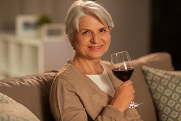 Canvas Print - people, alcohol and drinks concept - happy smiling senior woman drinking red wine from glass at home in evening