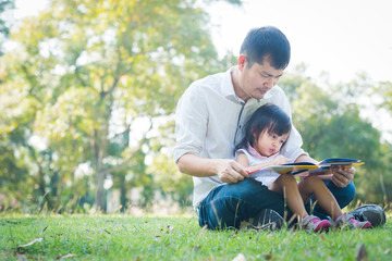 Wall Mural - Asian father and daughter are reading the book together in the park with fully happiness moment, concept of learning activity for kid in family lifestyle.