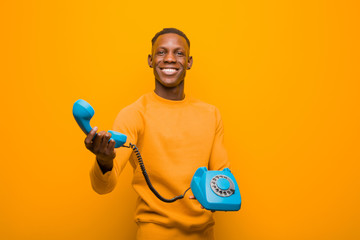 young african american black man against orange wall with a vintage telephone