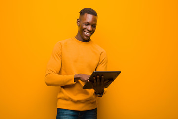 young african american black man against orange wall with a smart tablet