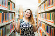 © Anna - Beautiful white woman female student in glasses smiling and looking on the camera and showing thumbs up. She is standing near, between bookshelves in modern interior library of university