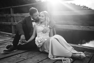 Black and white foto stylish couple of newlyweds posing on a bridge on wedding day. Handsome bearded groom admires and kisses pretty bride. Together. The concept of youth, love, fashion and lifestyle.