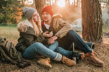 Travel couple camping with thermos in the forest. Concept of trekking, adventure and seasonal vacation.