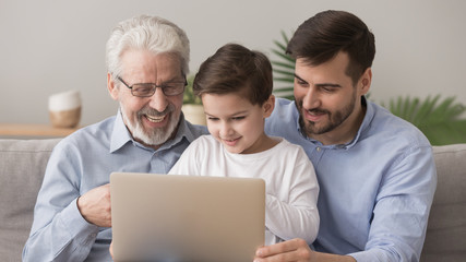 Wall Mural - Cute little boy with father and happy grandfather using laptop