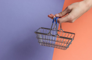 Wall Mural - Shopping concept. Female hand holds mini shopping basket on colored background