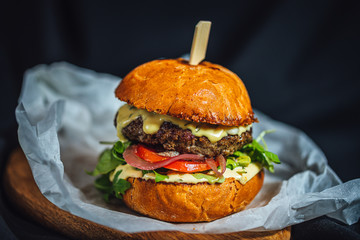 Homemade grilled beef burger with blue cheese and rucola served on wooden plate on dark background