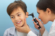 Little boy while ear exam. ENT doctor exam ear with otoscope on blue background