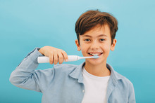 Mixed Race Little Boy Cleaning Teeth With Sonic Toothbrush On Blue Background. Perfect Removing Plaque With Cool Toothbrush