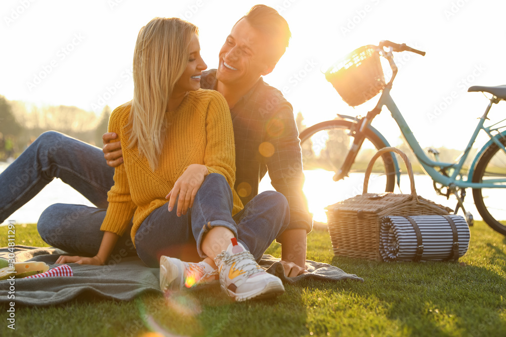 Happy young couple having picnic near lake on sunny day - obrazy, fototapety, plakaty 