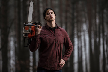 Lumberman working with chainsaw in the forest. Strong lumberjack with the chainsow in the forest.Stylish lumberman getting ready for work. Lifestyle.