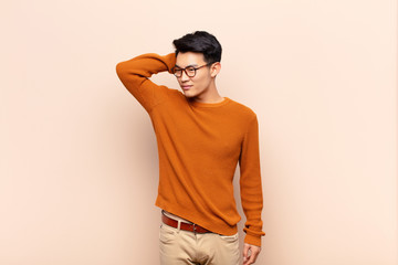 young chinese man smiling cheerfully and casually, taking hand to head with a positive, happy and confident look against flat color wall