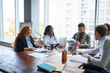 © alfa27 - multi-ethnic team of co-workers having a brainstorming session sitting around a table together with laptops in the office as they plan their business strategy for future work. Business people concept