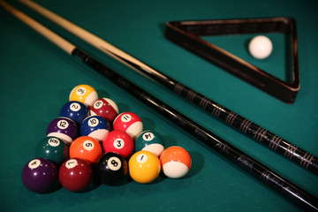 Sports game of billiards on a green cloth. Multi-colored billiard balls in the form of a triangle with numbers, two cues, a cue ball and a triangle on a pool table. Billiards billiard balls close up.