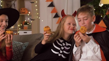 Sticker - halloween, holiday and childhood concept - smiling boy and girls in costumes eating cupcakes and having fun at home