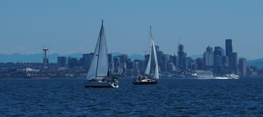 Wall Mural - Two sailboats sailing in front of Seattle skyline and waterfront area including Elliott Bay as seen looking from Elliott Bay