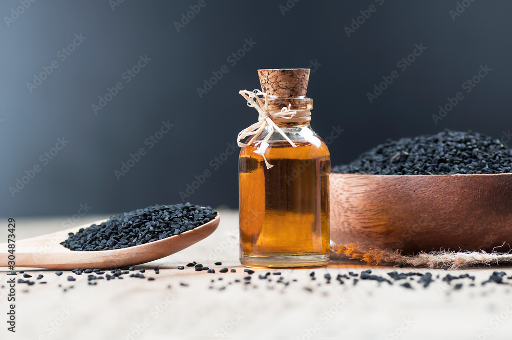 glass bottle of black cumin seeds essential oil , Nigella Sativa in spoon on wooden background. Organic herbal medicine for many diseases, black cumin - obrazy, fototapety, plakaty 