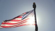 The American Flag Is Waving With A Bright Sun Behind