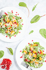 Wall Mural - Fresh green organic salad with raw ingredients close up. Tasty salad with arugula, orange slices, pomegranate and cheese on white plate, top view. Healthy eating, dieting concept