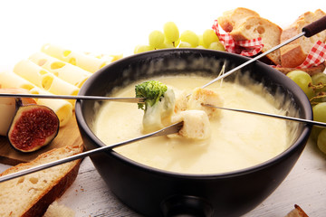 Gourmet Swiss fondue dinner on a winter evening with assorted cheeses on a board alongside a heated pot of cheese fondue with two forks dipping