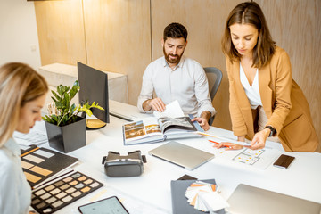 Wall Mural - Young employees dressed casually doing some creative work at the large table with computers in the office. Concept of an architectural business and creative work