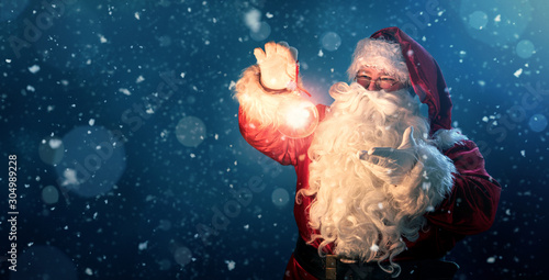 Photographie Happy Santa Claus holding glowing christmas ball over defocused blue background