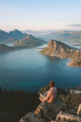 Wall Mural - Traveler man sitting alone on mountain cliff adventure hiking healthy lifestyle vacations view from above Lofoten islands sea in Norway