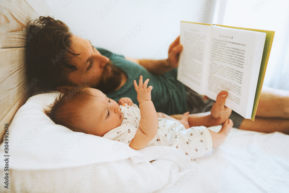 Family father and infant baby reading book fairytale laying on bed at home lifestyle dad and child daughter together parenthood childhood concept Fathers day holiday - obrazy, fototapety, plakaty 