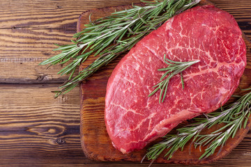 Raw Fresh Steak Served with Twigs of Rosemary on Rustic Wooden Board. Marbled Meat with Ingredients for Cooking. Top View