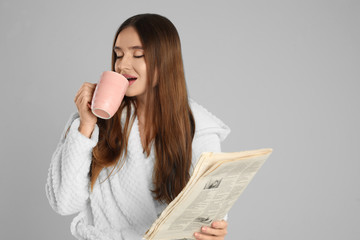 Canvas Print - Beautiful young woman in bathrobe with cup of coffee on light grey background