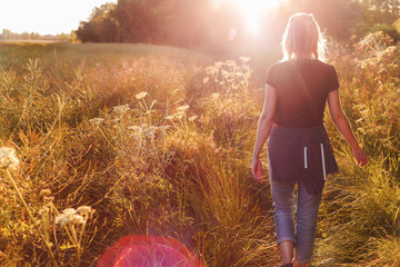 Beautiful young woman walking in field with sunrise