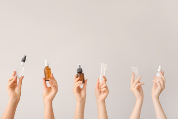 female hands with different cosmetic products in bottles on grey background