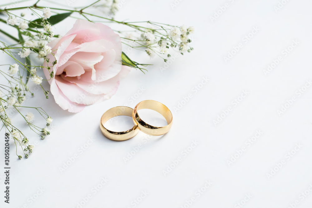 Pink flowers and two golden wedding rings on white background. - obrazy, fototapety, plakaty 