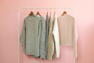 Wall Mural - Warm sweaters on a wardrobe hanger on a colored background. Autumn, winter clothes.