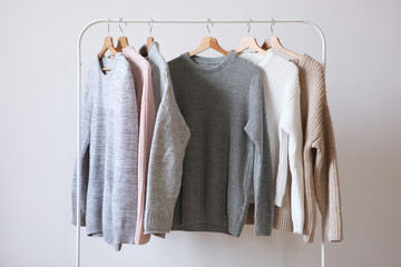 Wall Mural - Warm sweaters on a wardrobe hanger on a light background. Autumn, winter clothes.