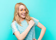 young pretty blonde woman feeling happy, positive and successful, motivated when facing a challenge or celebrating good results against flat color wall