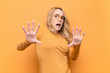 © kues1 - young pretty blonde woman feeling terrified, backing off and screaming in horror and panic, reacting to a nightmare against flat color wall