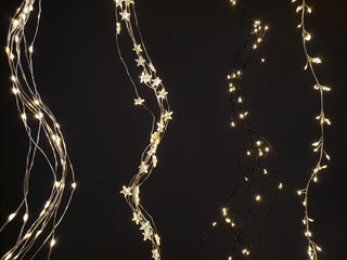 Wall Mural - Star and sleeve Christmas lights, fairy lights hanging in a wave form next to each other on dark background.