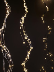 Wall Mural - Star and sleeve Christmas lights, fairy lights hanging in a wave form next to each other on dark background.