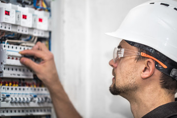 Wall Mural - Man, an electrical technician working in a switchboard with fuses. Installation and connection of electrical equipment. Close up.