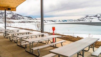 Wall Mural - Panorama Picnic pavilion overlooking a snowy winter landscape of lake and mountain