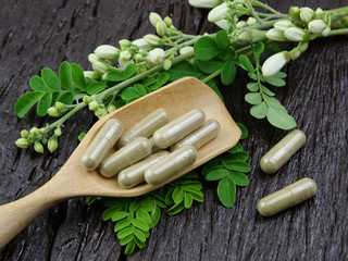 Moringa capsules on a wooden spoon and flowers on a wooden table.