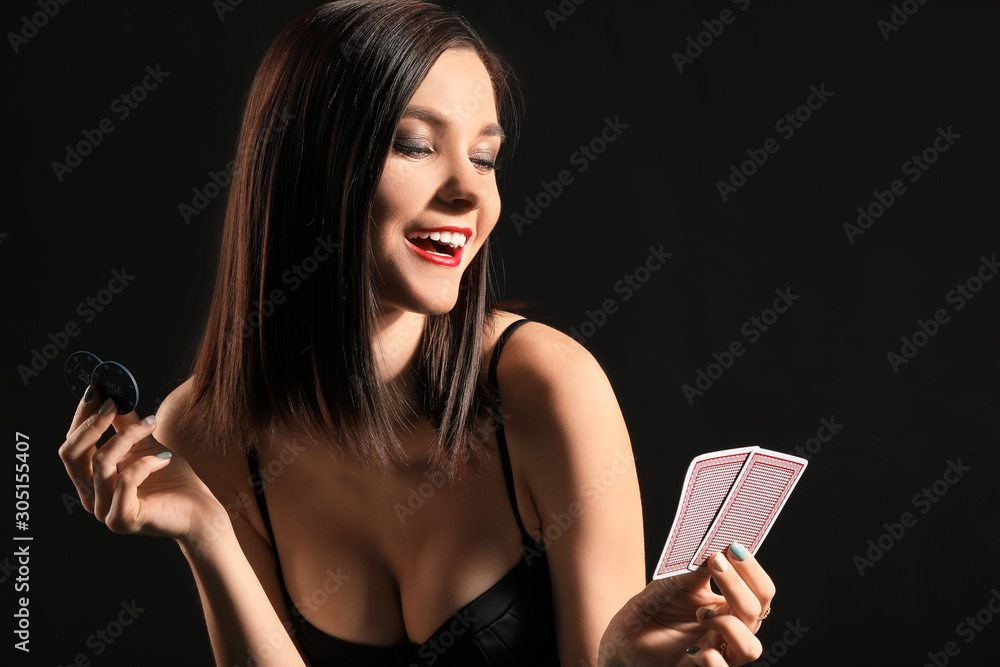 Beautiful young woman with playing cards and chips on dark background
