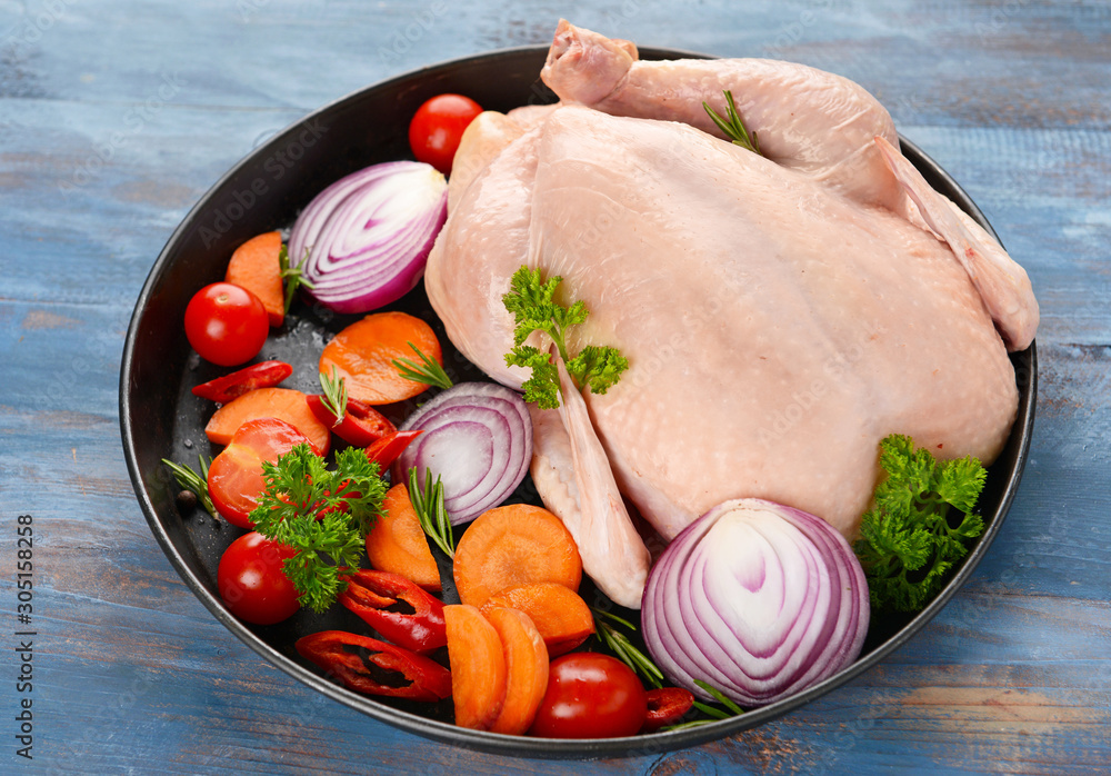 Frying pan with raw chicken and vegetables on wooden background