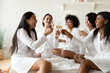 © fizkes - Excited diverse girls friends wear robes celebrating clinking champagne glasses
