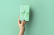 Female hand with turquoise gift box on color background
