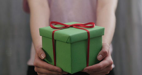 young woman stand and show green gift box with red ribbon bow