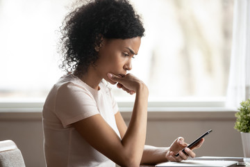 Pensive african American woman lost in thoughts using cellphone